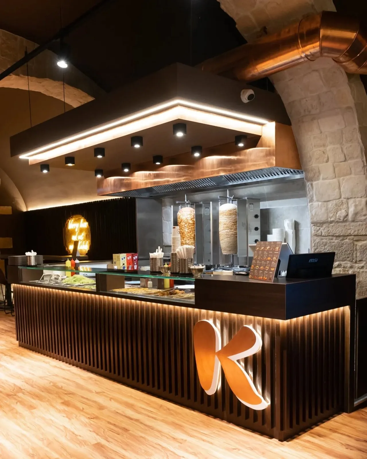 Dentro un ristorante Kebabberia: archi in pietra, bancone illuminato e la grande K